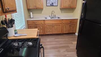 A kitchen with wooden cabinets, a black stove, a sink, and a refrigerator.