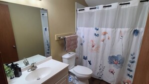 Een badkamer met een witte wastafel, spiegel en toilet. Er is een douchegordijn met bloemenmotieven.