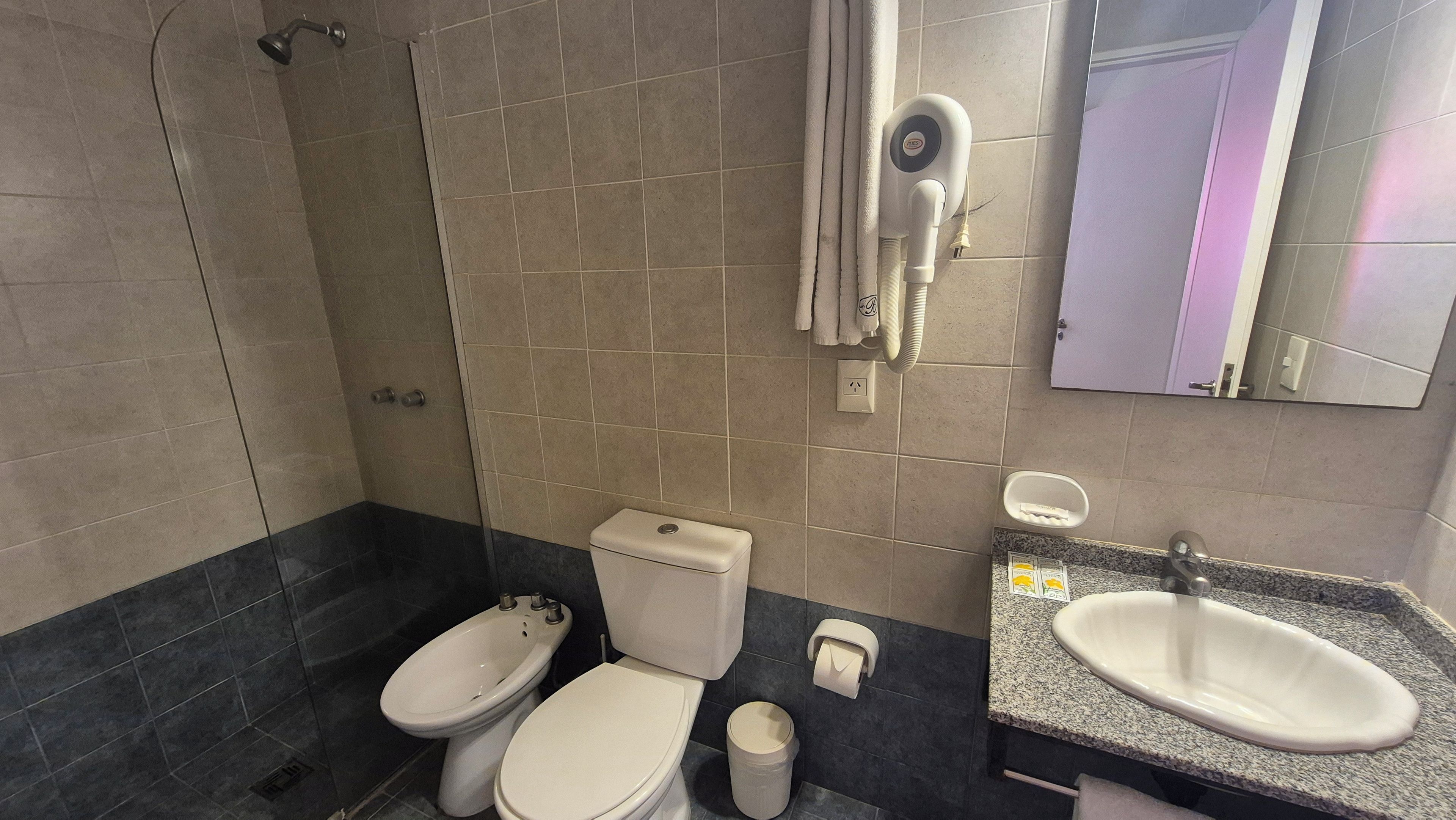 Un baño con ducha, dos inodoros, un lavabo y un espejo.