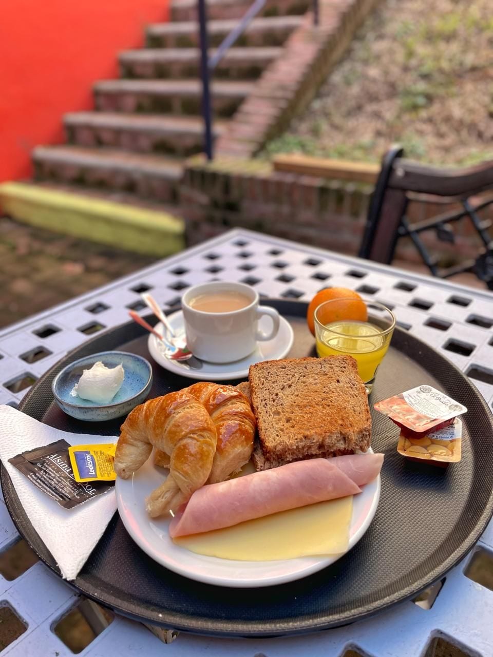 Un plateau avec des croissants, du jambon, du fromage, une tasse de café, une orange et un petit pot de beurre.