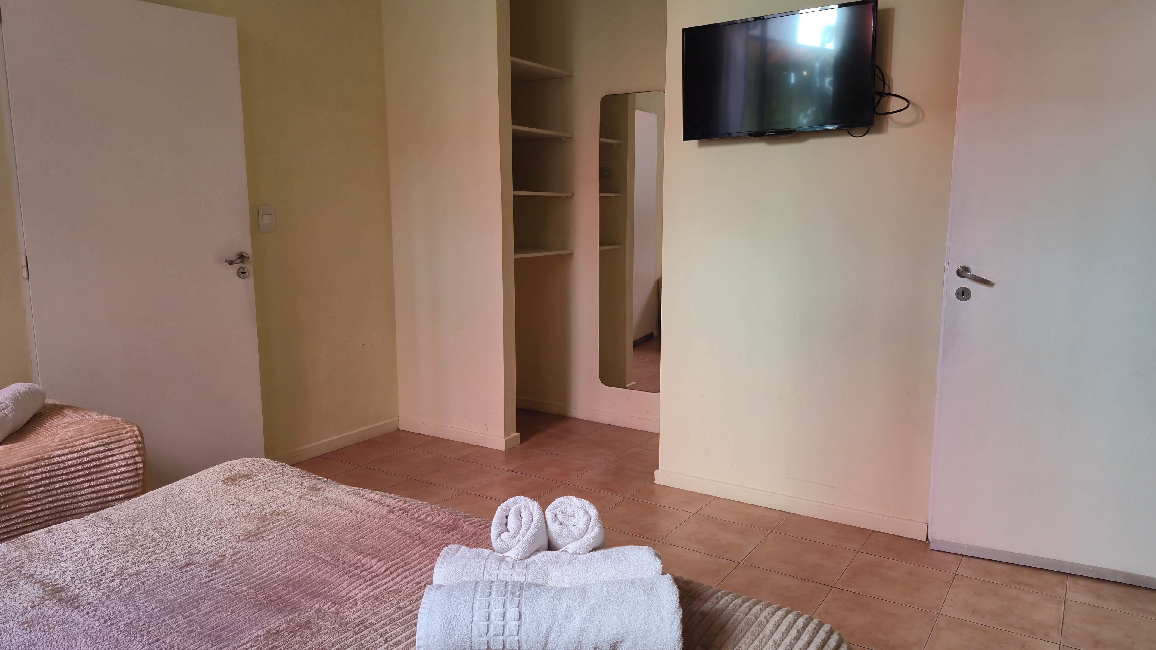 A hotel room with a bed, a TV mounted on the wall, a closet, and a bathroom door.