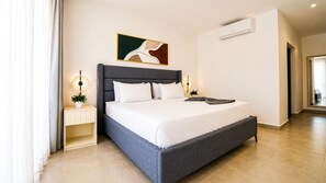 Ein modernes Hotelzimmer mit einem großen Bett, Nachttischlampen, einem kleinen Tisch mit einer Pflanze und einem Gemälde an der Wand.