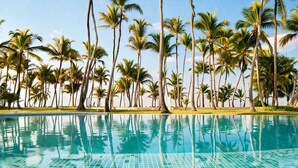 A swimming pool with clear blue water, surrounded by tall palm trees and a clear sky. - Wake Up to the Ocean: 3-Bedroom Palmera · Beach & Pool (Punta Cana)