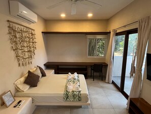 A hotel room with a bed, bedside table, desk, and a view of the outdoors. - Casa Parota (Ixtapa Zihuatanejo)