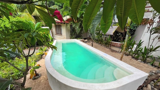 Ein rechteckiger Pool mit klarem Wasser, umgeben von Sand und tropischen Pflanzen.