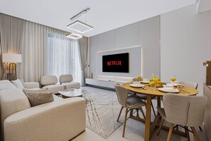 Ein modernes Wohnzimmer mit Essbereich, einer Sofagarnitur, einem an der Wand befestigten Fernseher und einem für das Frühstück gedeckten Tisch.