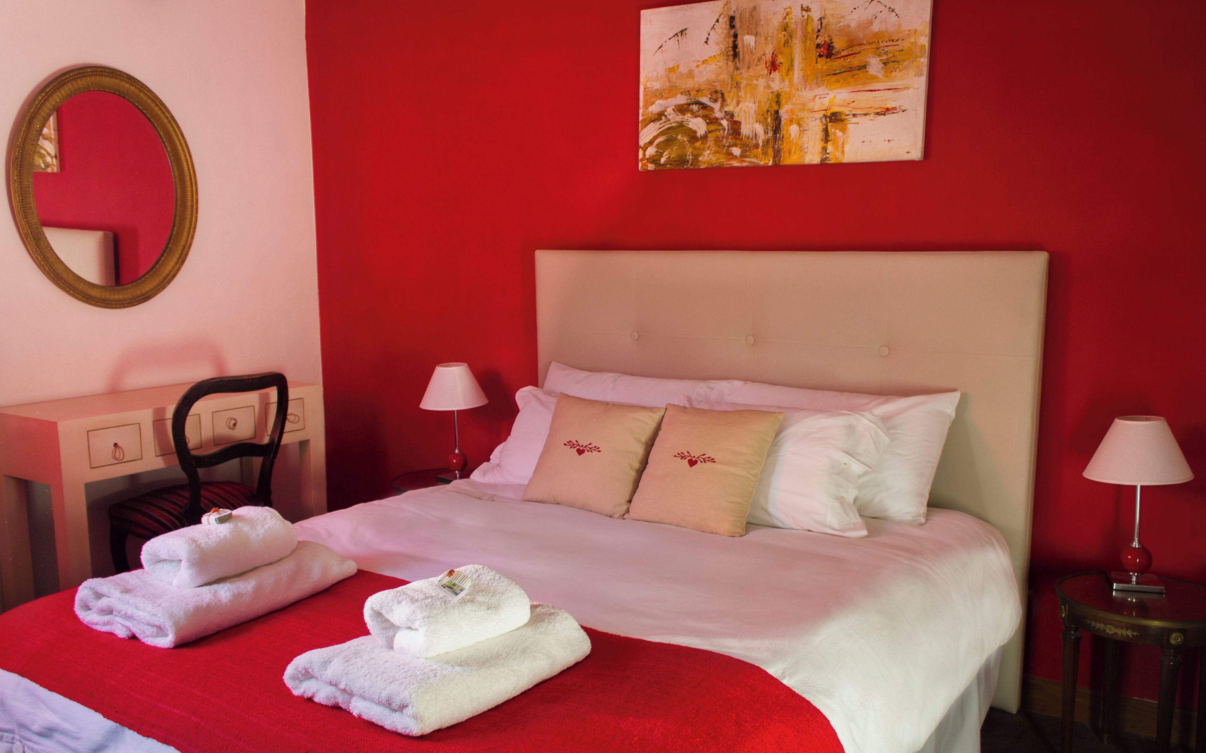 A hotel room with a bed, two bedside tables, a chair, a mirror, and a painting on the wall.