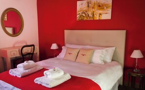 Une chambre d’hôtel avec un lit, deux tables de chevet, une chaise, un miroir et un tableau au mur.