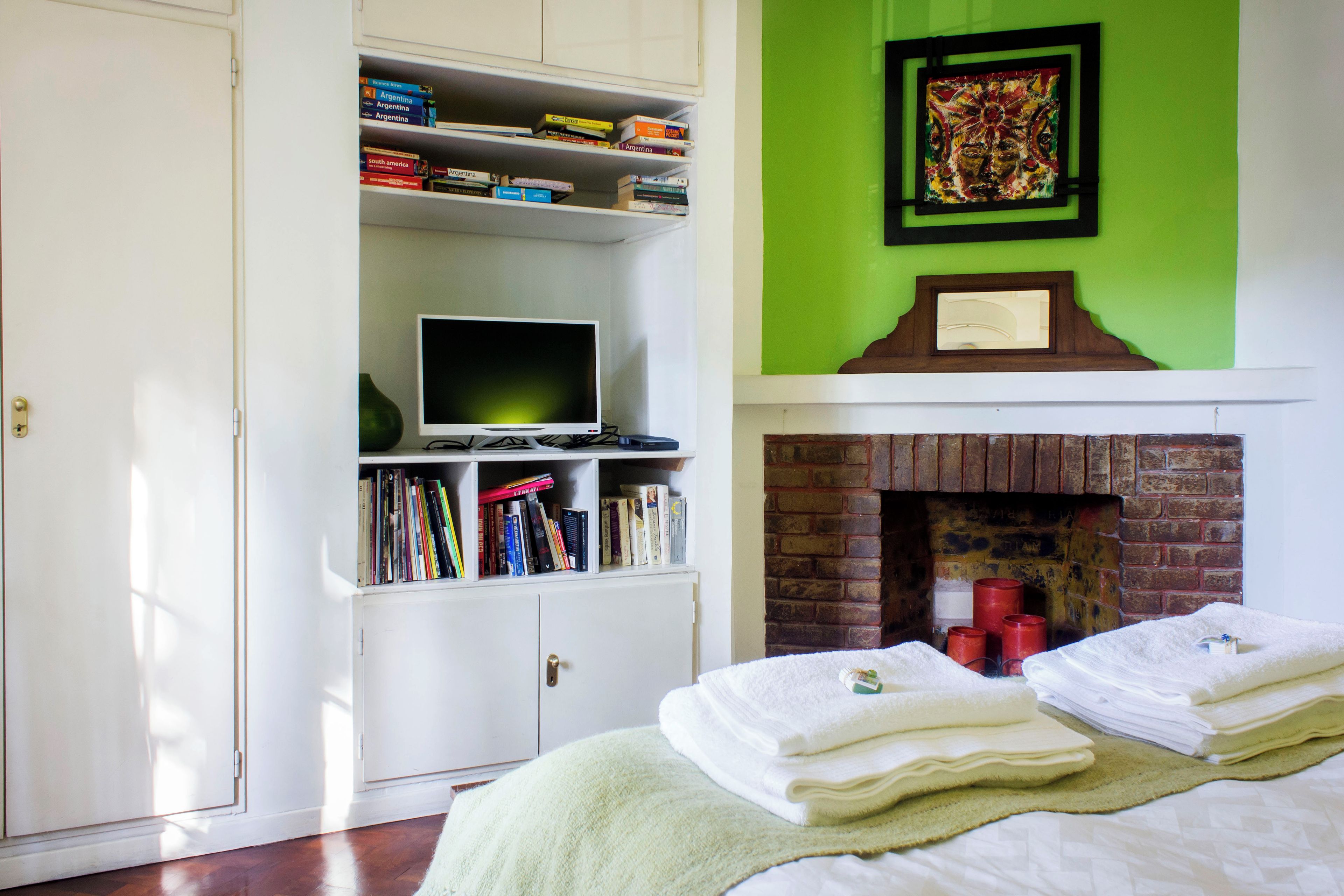 A bedroom with a bed, a bookshelf, a television, a fireplace, and a green wall.