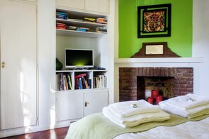 A bedroom with a bed, a bookshelf, a television, a fireplace, and a green wall.