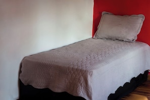A single bed with a quilted bedspread and a pillow against a wall with a red accent.
