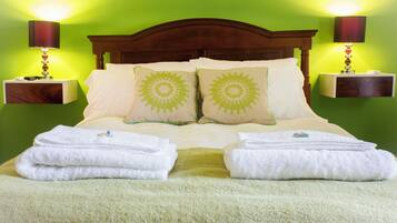 Una cama bien tendida con dos almohadas, dos mesitas de noche con lámparas y una pared verde.