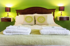 Un lit bien fait, avec deux oreillers, deux tables de chevet avec des lampes et un mur vert.