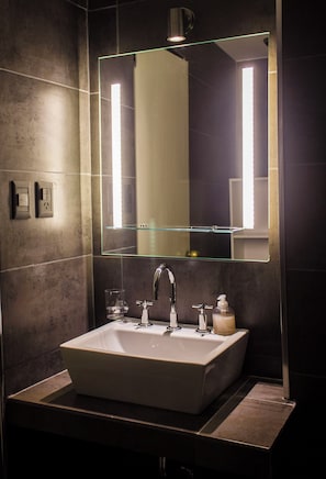 Une salle de bain avec un miroir rectangulaire, un lavabo, un robinet, un distributeur de savon et un verre.