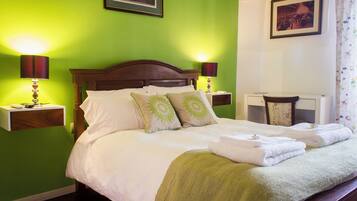 Una cama bien hecha con sábanas blancas y almohadas verdes, dos lámparas de noche y un cuadro colgado encima de la cama.