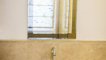 Un baño con un lavamanos blanco, un espejo encima y una ventana con cortinas florales.