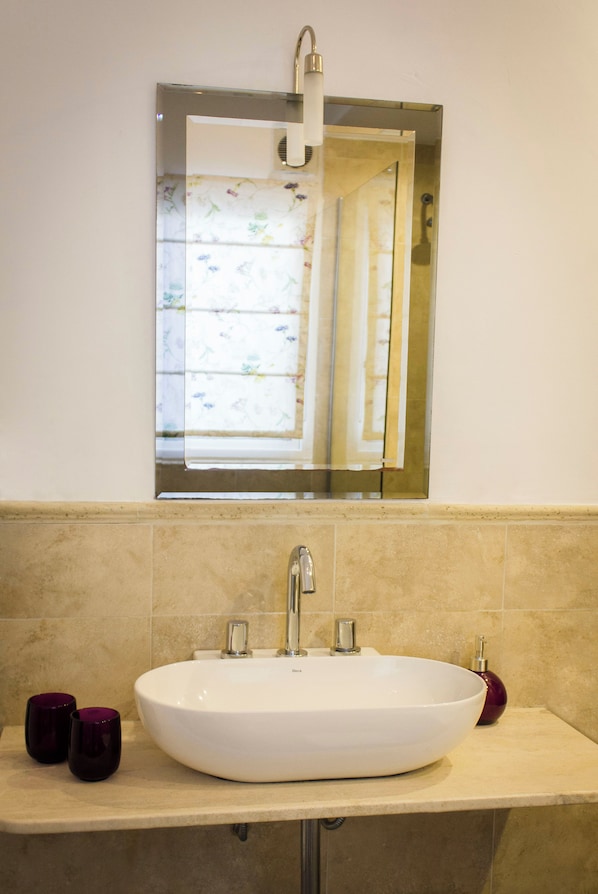 Une salle de bain avec un lavabo blanc, un miroir au-dessus et une fenêtre ornée de rideaux à motifs floraux.