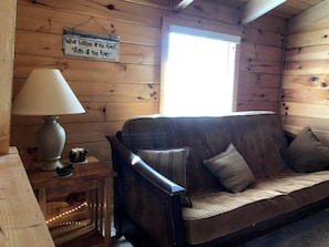 A wooden cabin interior with a sofa, a lamp, and a sign on the wall. - Rustic Cabin Rental near the Gauley River in West Virginia (Hico)