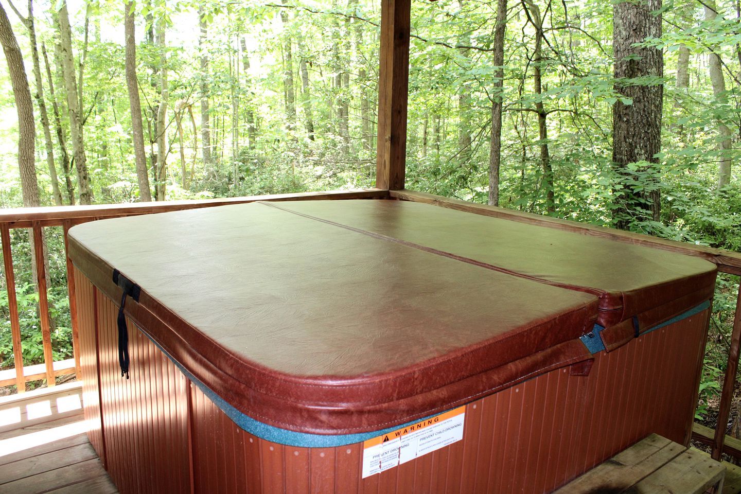 Jacuzzi con cubierta de madera y una etiqueta de advertencia en el lateral.