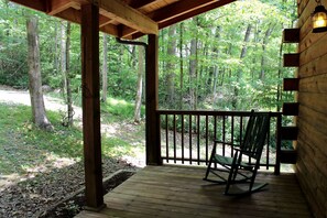 A wooden porch with a rocking chair, surrounded by a forested area. - Rustic Cabin Rental near the Gauley River in West Virginia (Hico)