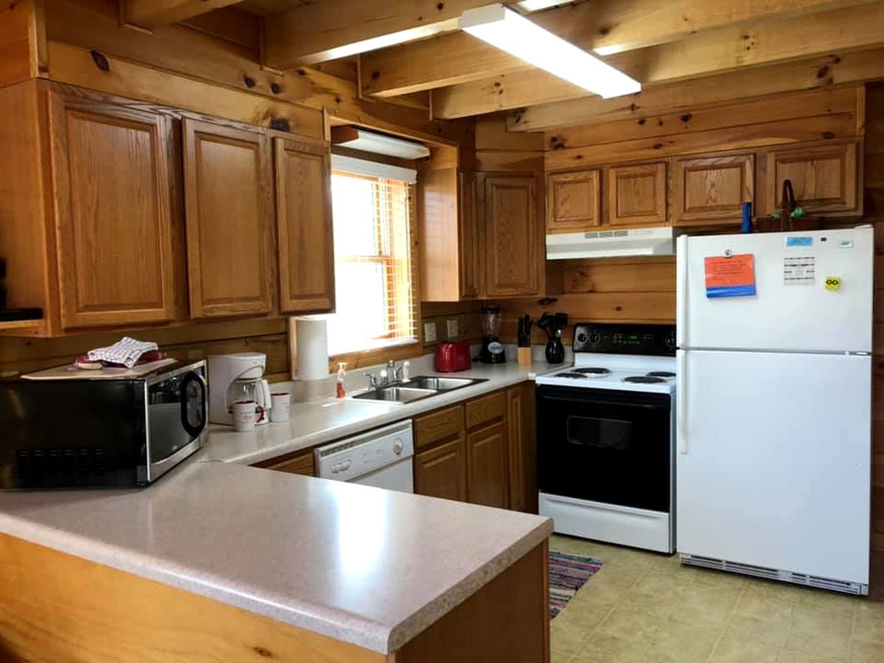 Una cocina con armarios de madera, microondas, refrigerador, estufa y pileta.