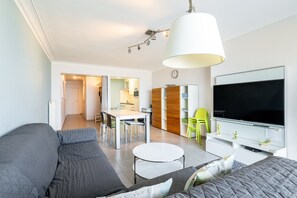 A modern living room with a sofa, a dining table, and a TV. - Apartment in Blankenberge With Sea Views (Blankenberge)