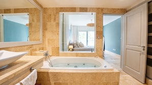 A modern bathroom with a freestanding bathtub, a large mirror, and a view into a bedroom through a glass door. - The Ocean Is Your Window: 2-Bedroom Apartment at Playa Palmera (Punta Cana)