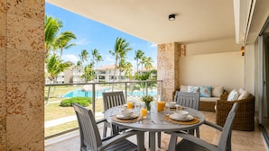 A balcony with a table set for breakfast, overlooking a pool and palm trees. - The Ocean Is Your Window: 2-Bedroom Apartment at Playa Palmera (Punta Cana)