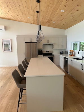 Cocina moderna con una isla central, techo de madera y muebles altos blancos.