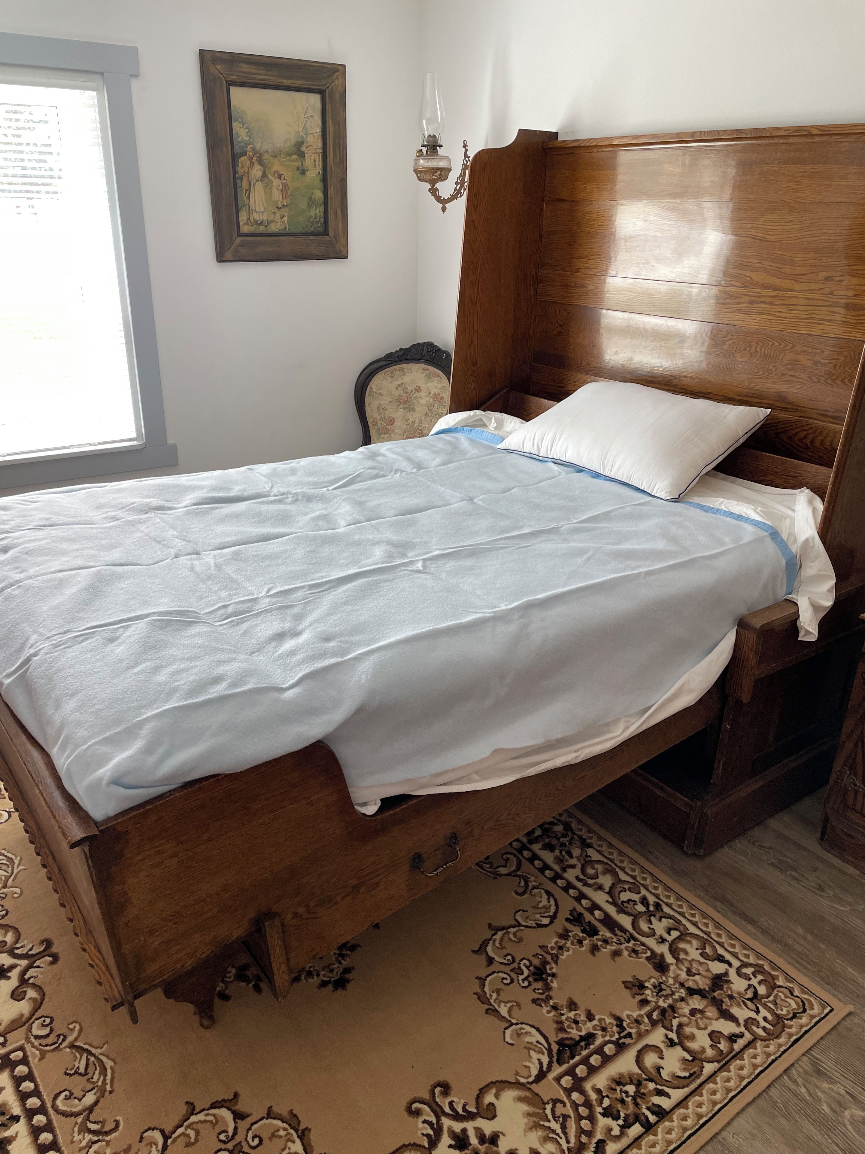 A wooden bed with a white and blue bedspread, a white pillow, and a wooden headboard.