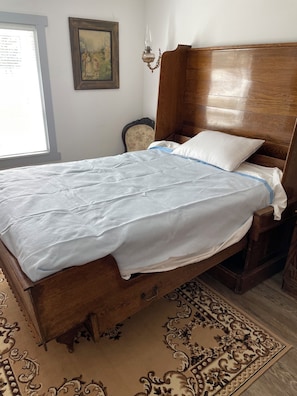 A wooden bed with a white and blue bedspread, a white pillow, and a wooden headboard.