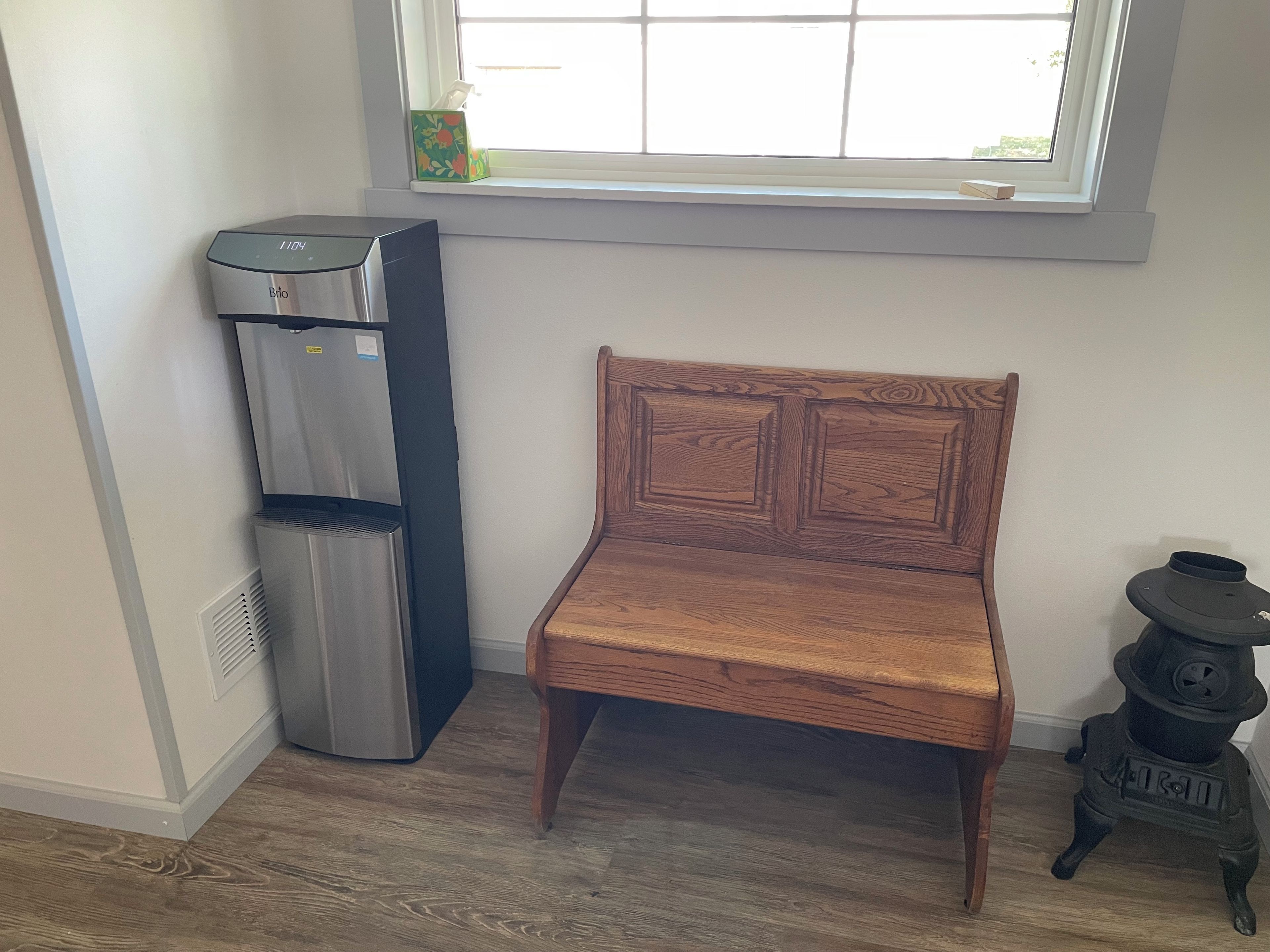 A room with a wooden bench, a water dispenser, and a stove.