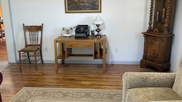 Ein Zimmer mit einem Holztisch, einem Stuhl, einem gemusterten Sofa, einem Holzschrank und einem Bild an der Wand.