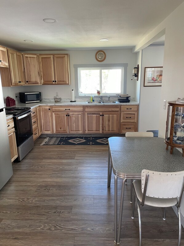 A kitchen with wooden cabinets, a microwave, a stove, a sink, and a dining table with chairs.