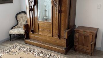 Een kamer met een groot houten kast, een stoel met bloemenstoffering, een klein houten bijzettafeltje en een kamerbreed tapijt op de vloer.