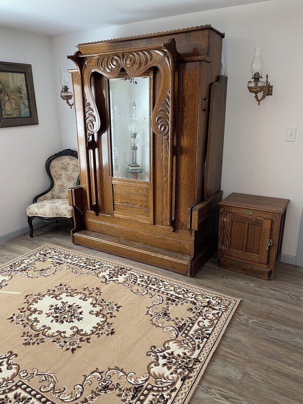 A room with a large wooden cabinet, a chair with floral upholstery, a small wooden side table, and a patterned rug on the floor.