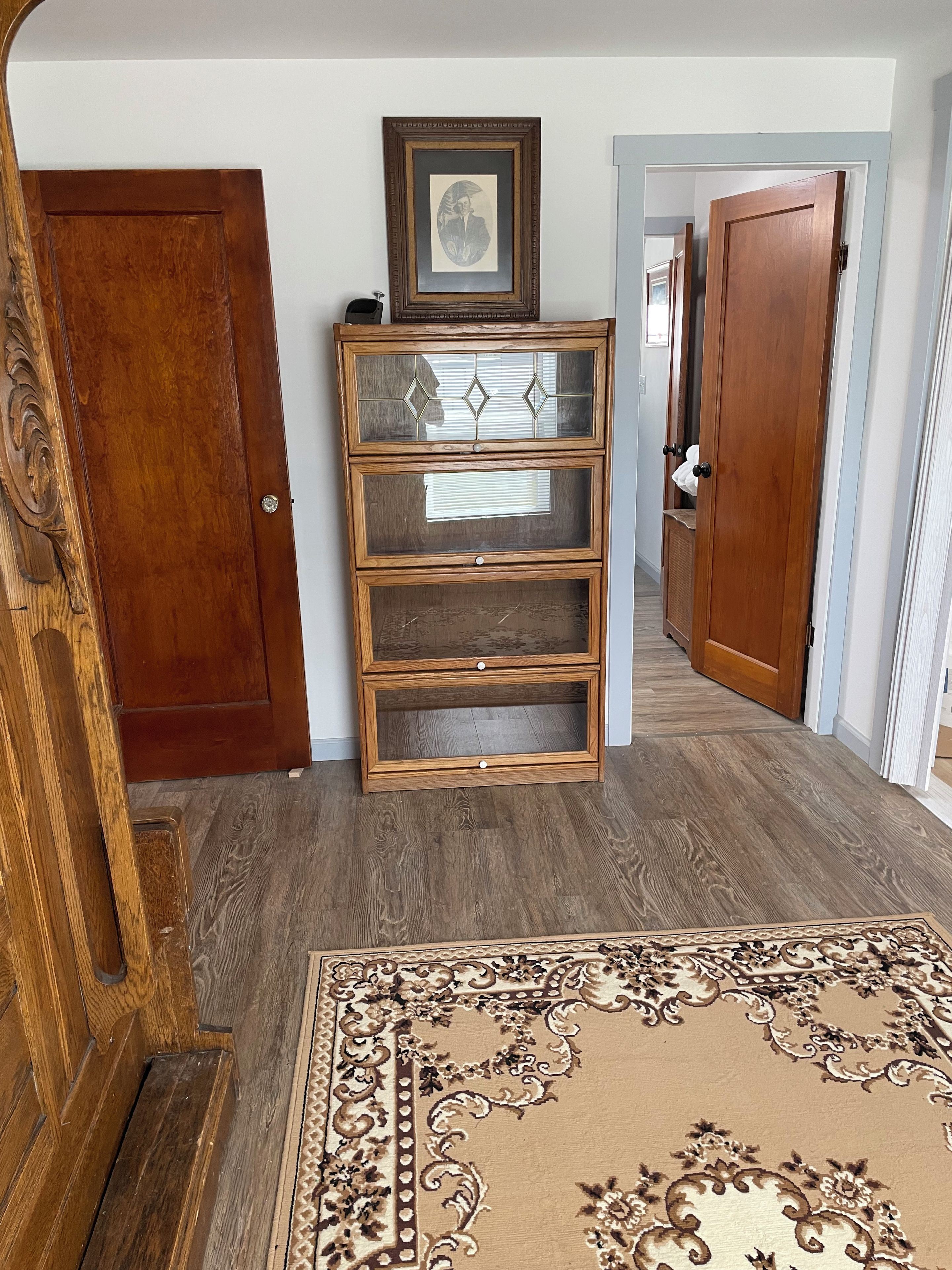 A hallway with a wooden door, a wooden cabinet with glass doors, and a patterned rug.
