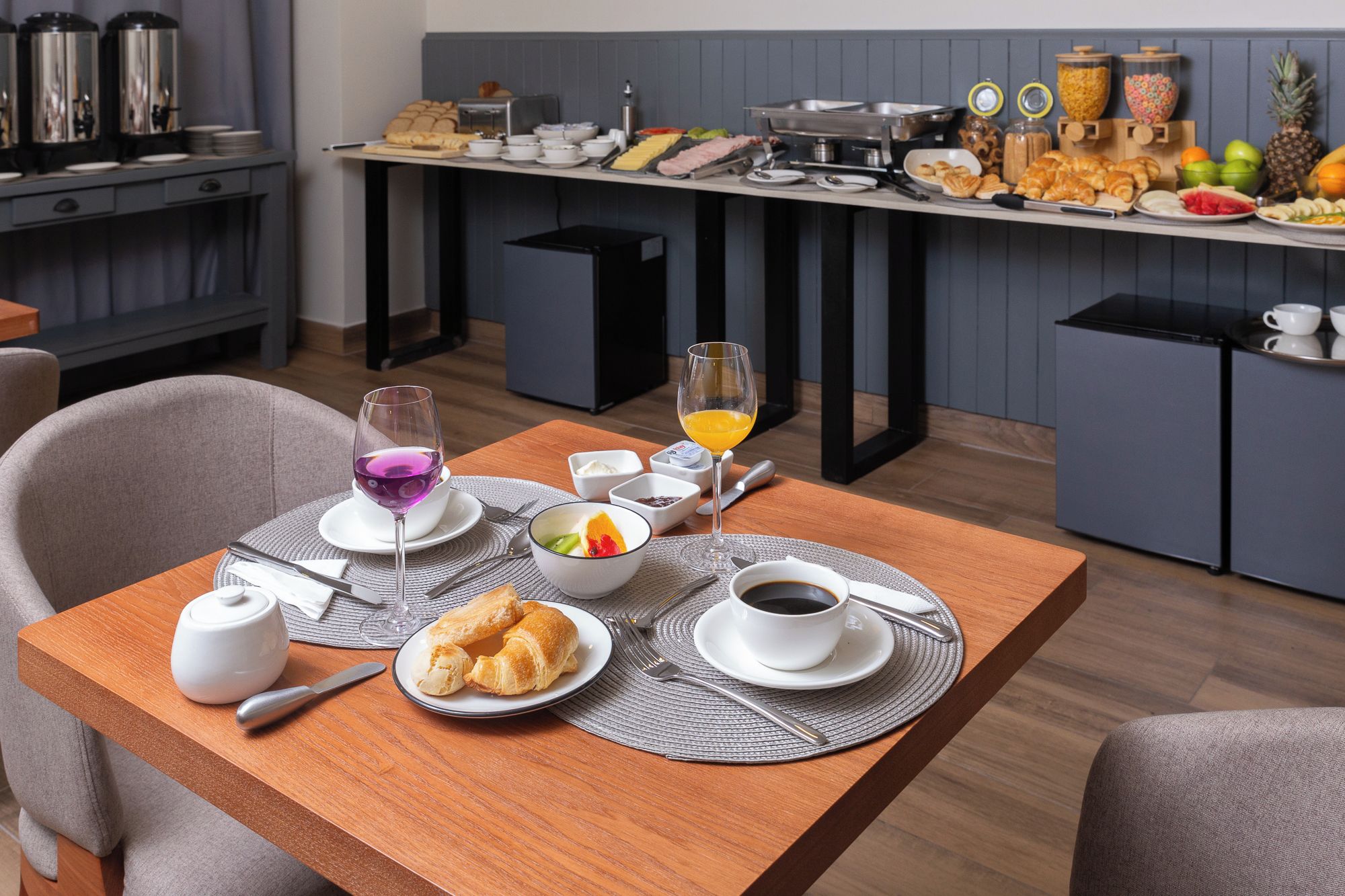Disposição para o café da manhã com croissants, um copo de suco de laranja e uma tigela de frutas.