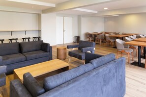 Un espacio lounge moderno con sofás, una mesa de centro y una zona de comedor con mesas y sillas.