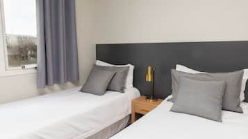A hotel room with two single beds, a bedside table with a lamp, and a window with curtains.
