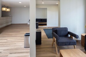 Un interior moderno con suelo de madera, un sofá negro, un sillón azul y una pequeña mesa de madera.