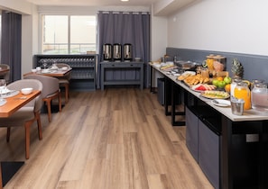 Cocina compacta con comedor, equipada con cafetera, frutero y diversos productos para el desayuno.