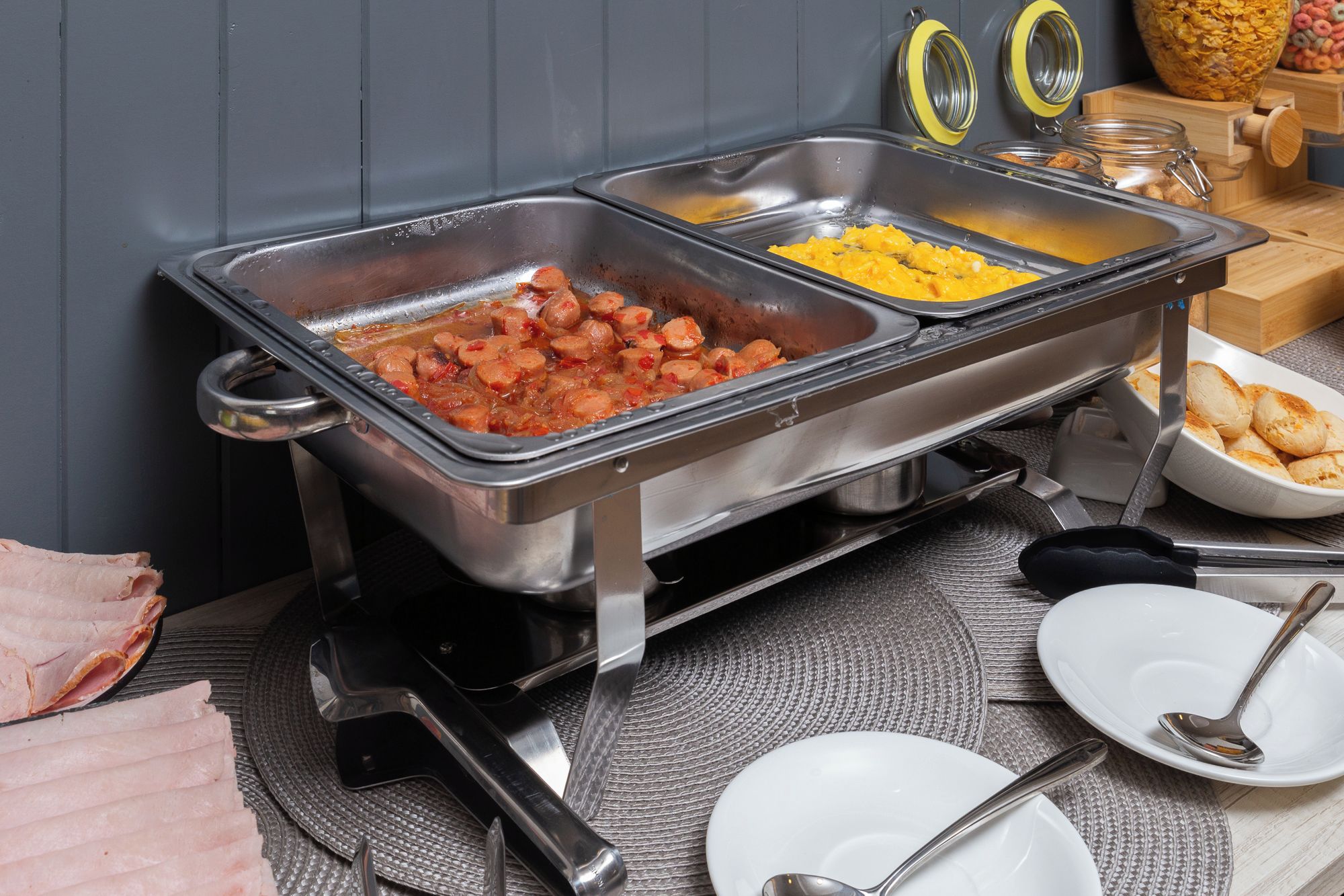 Un buffet proposant une variété de plats, notamment des saucisses, des œufs brouillés et des viennoiseries.