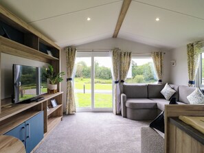 Ein modernes Wohnzimmer mit einer Couch, einem Fernseher und Blick auf eine grüne Landschaft durch große Fenster.