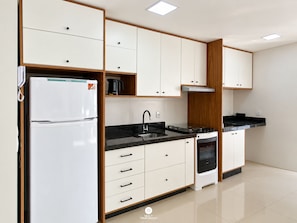 A modern kitchen with white cabinetry, a built-in oven, and a refrigerator. - Ap Blue Garden 800mt da Praia - Itapema/sc (Itapema)