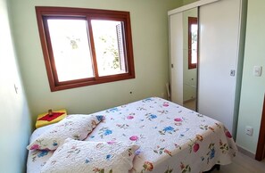 Un dormitorio con una cama individual, una ventana con persianas, un armario y una pequeña mesa con un florero.