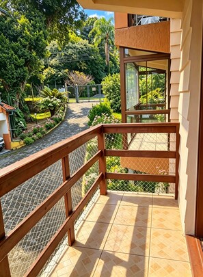 Un balcón con baranda de madera, suelo de baldosas y vista a un jardín ajardinado con diversas plantas y un sendero.