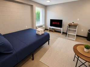 A room with a single bed, a TV, a small table with a plant, and a window with blinds. - The Foundry Studio | Downtown Retreat U3 (Birmingham)