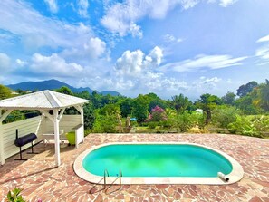 Una piscina con solárium de piedra, zona de estar techada y vistas a un paisaje montañoso.