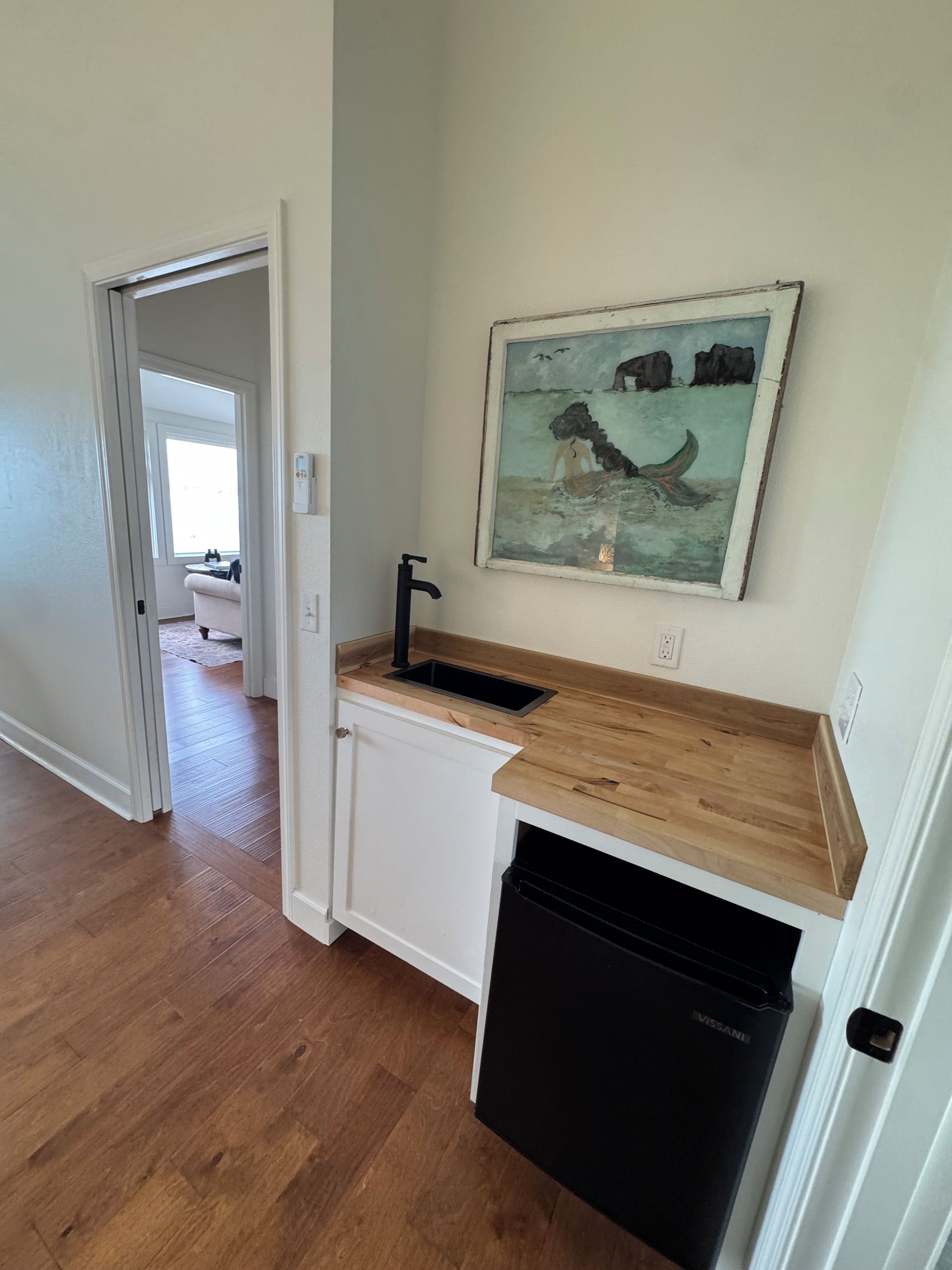 A kitchen with a wooden countertop, a black dishwasher, and a painting of a dog on a boat.